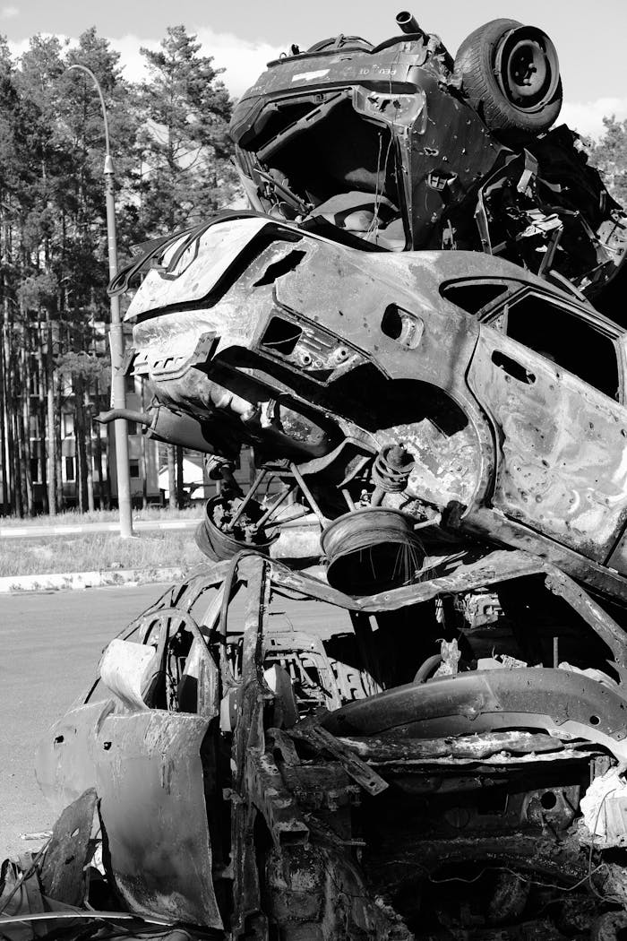 Services Vertical black-and-white photo of stacked junked cars in an outdoor scrapyard.