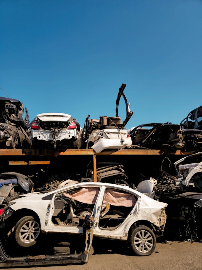 Home Rows of damaged vehicles in a scrapyard under a clear blue sky.