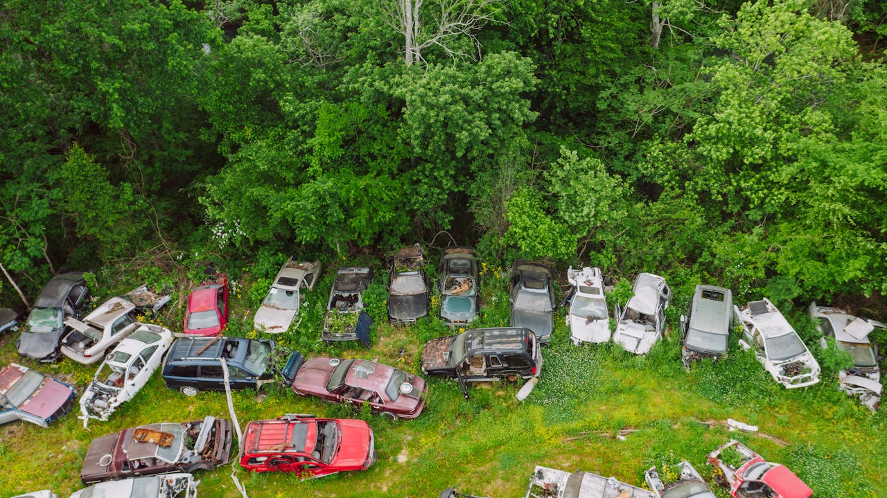 About From above of various crashed cars on car dump on green grass near forest in summer day